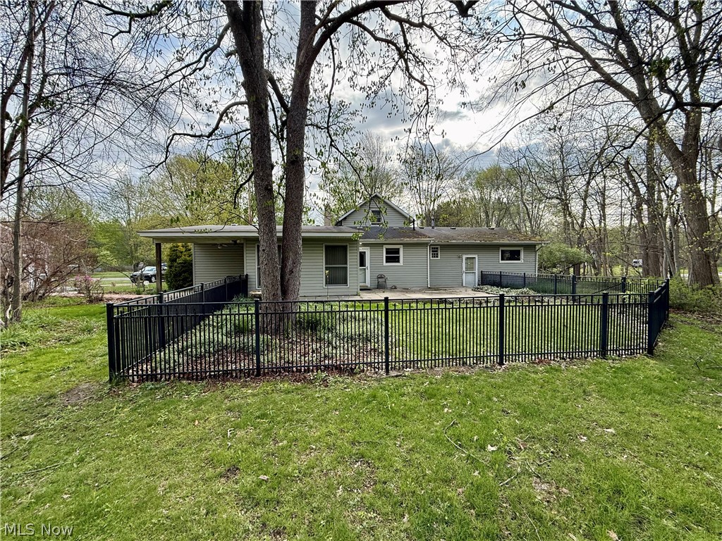 6066 Case Road North Ridgeville, OH 44039 - Photo 4 of 19 Single-story residential structure with light-colored siding, a covered patio area, and a black metal fence enclosing a portion of the yard