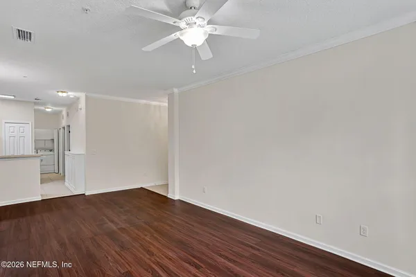 a view of an empty room with wooden floor and a ceiling fan