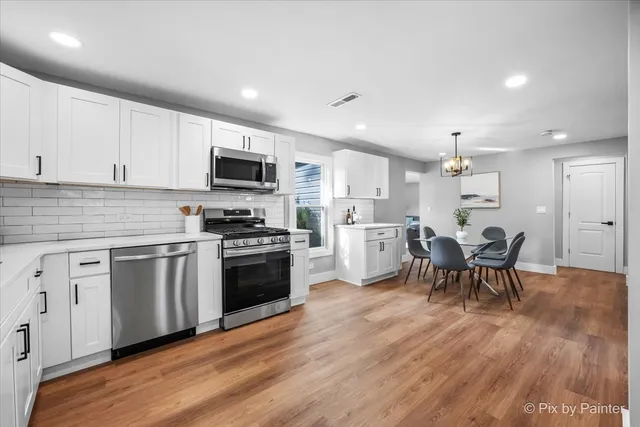 a kitchen with stainless steel appliances kitchen island granite countertop a stove top oven a sink a dining table and chairs with wooden floor