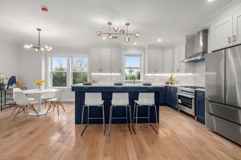 a kitchen with granite countertop a refrigerator a stove a dining table and chairs with wooden floor