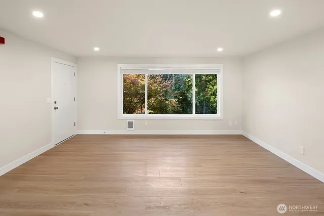 a view of an empty room with wooden floor and a window