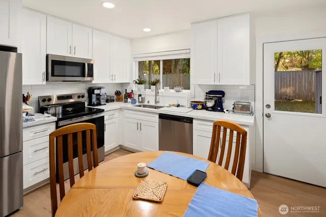 a kitchen with stainless steel appliances granite countertop a sink a stove a refrigerator cabinets and a dining table with wooden floor