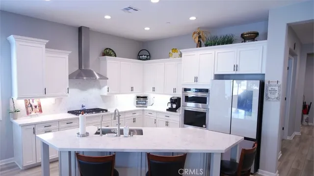 a kitchen with stainless steel appliances granite countertop a sink a stove a refrigerator and white cabinets with wooden floor