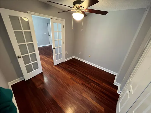 a view of an empty room with wooden floor and a ceiling fan