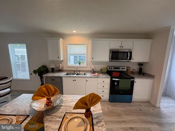 a kitchen with stainless steel appliances granite countertop a stove top oven a sink dishwasher and white cabinets with wooden floor