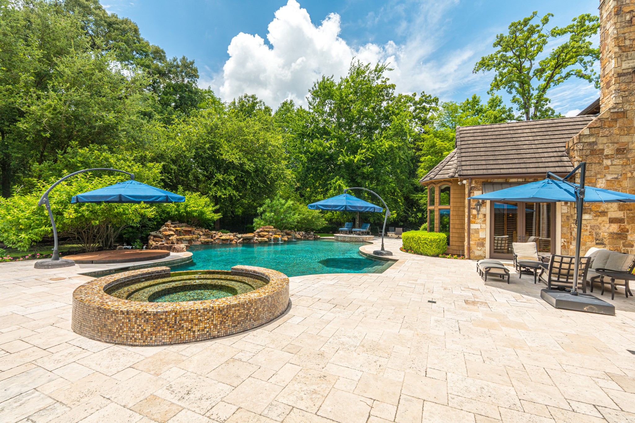 247 South Fazio Way Spring, TX 77389 - Photo 11 of 17 Designed for effortless entertaining, this remarkable backyard retreat features an impressive travertine patio, elevated spa, custom pool, and multiple lounge areas, all within a serene wooded setting that creates a a true outdoor sanctuary.