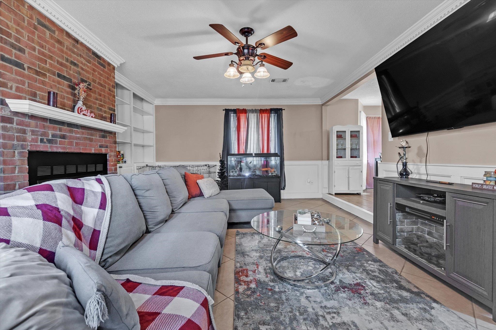 480 Friars Point Lane Memphis, TN 38018 - Photo 7 of 26 Living room with a wainscoted wall, crown molding, ceiling fan, light tile patterned flooring, and a brick fireplace