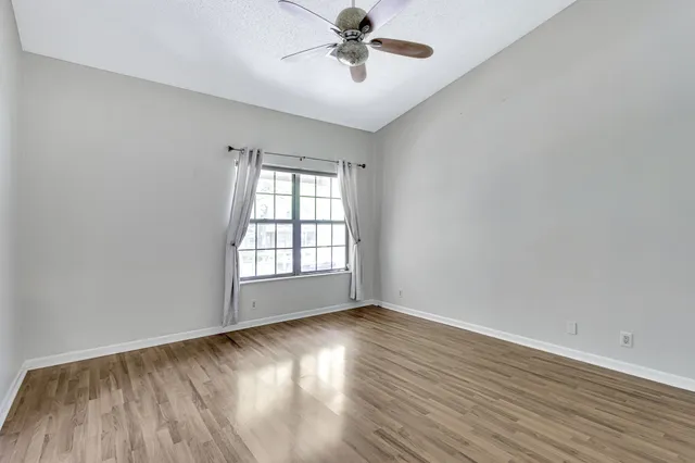 an empty room with wooden floor chandelier fan and windows