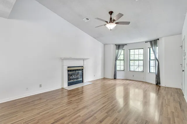 an empty room with wooden floor fan and windows