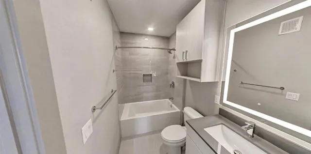 a bathroom with a granite countertop bathtub shower sink vanity mirror and toilet