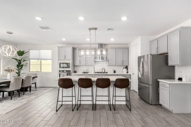 a kitchen with stainless steel appliances a table chairs refrigerator and wooden floor