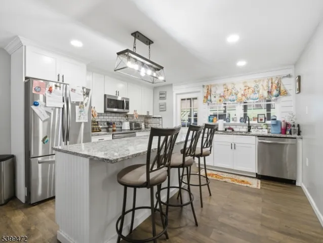 a kitchen with stainless steel appliances granite countertop a refrigerator a stove top oven a sink dishwasher and white cabinets with wooden floor