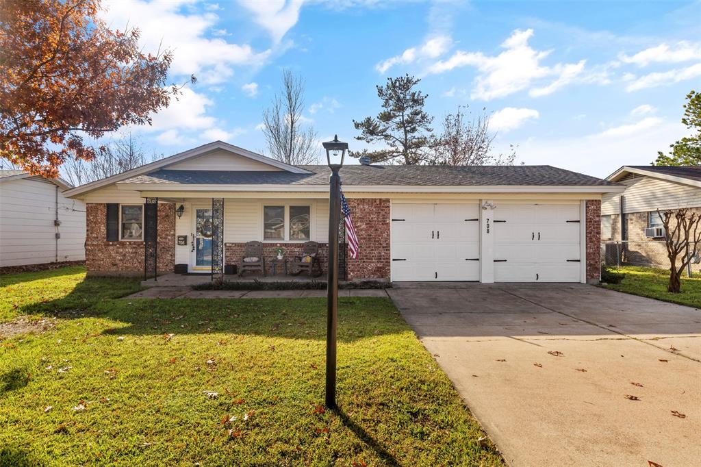 Exterior featuring brick and siding facade, covered front porch, a two-car garage with white doors, a paved driveway, and a manicured lawn