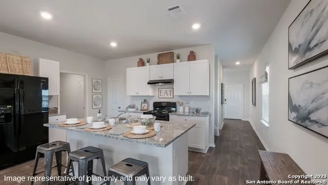 a kitchen with stainless steel appliances kitchen island granite countertop a refrigerator a stove a sink a dining table and chairs with wooden floor