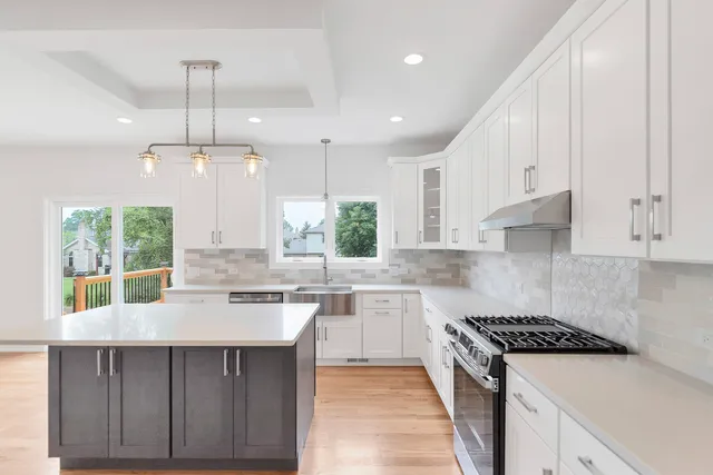 a large kitchen with stainless steel appliances a stove a refrigerator a sink and white cabinets with wooden floor