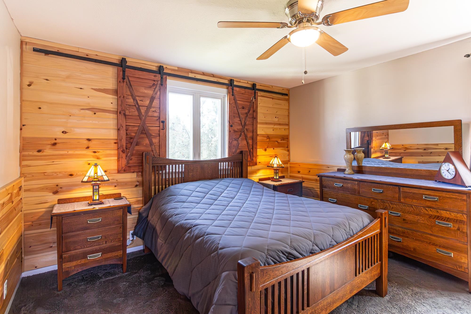 1151 East Camp Street Ely, MN 55731 - Photo 26 of 45 Carpeted bedroom with ceiling fan, wooden walls, and a barn door