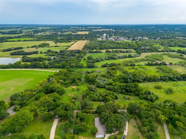 an aerial view of a residential houses with outdoor space and trees all around