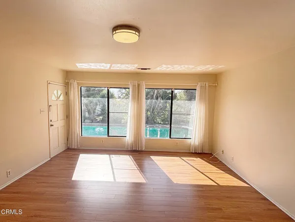 a view of an empty room with wooden floor and a window