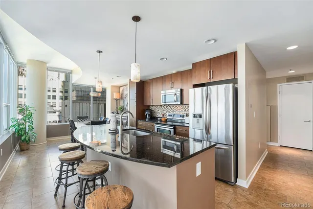 a kitchen with stainless steel appliances kitchen island granite countertop a refrigerator a oven a sink and a dining table with wooden floor