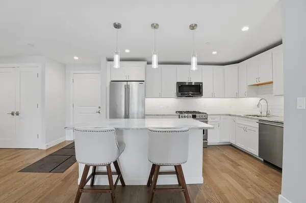 a kitchen with stainless steel appliances granite countertop a stove a sink a microwave a refrigerator and white cabinets with wooden floor