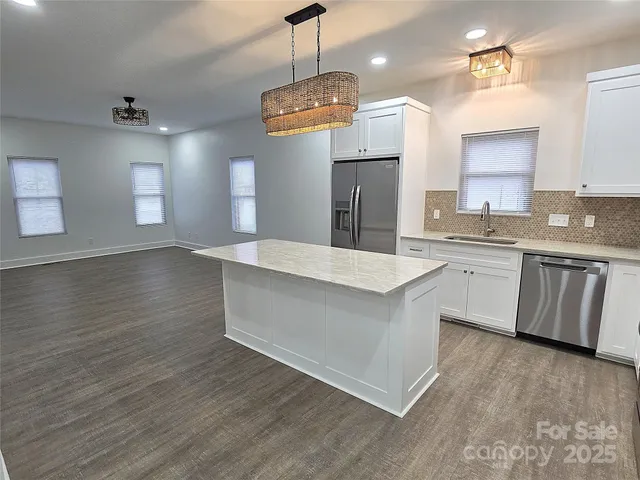a kitchen with stainless steel appliances granite countertop a sink a stove a refrigerator and island with wooden floor
