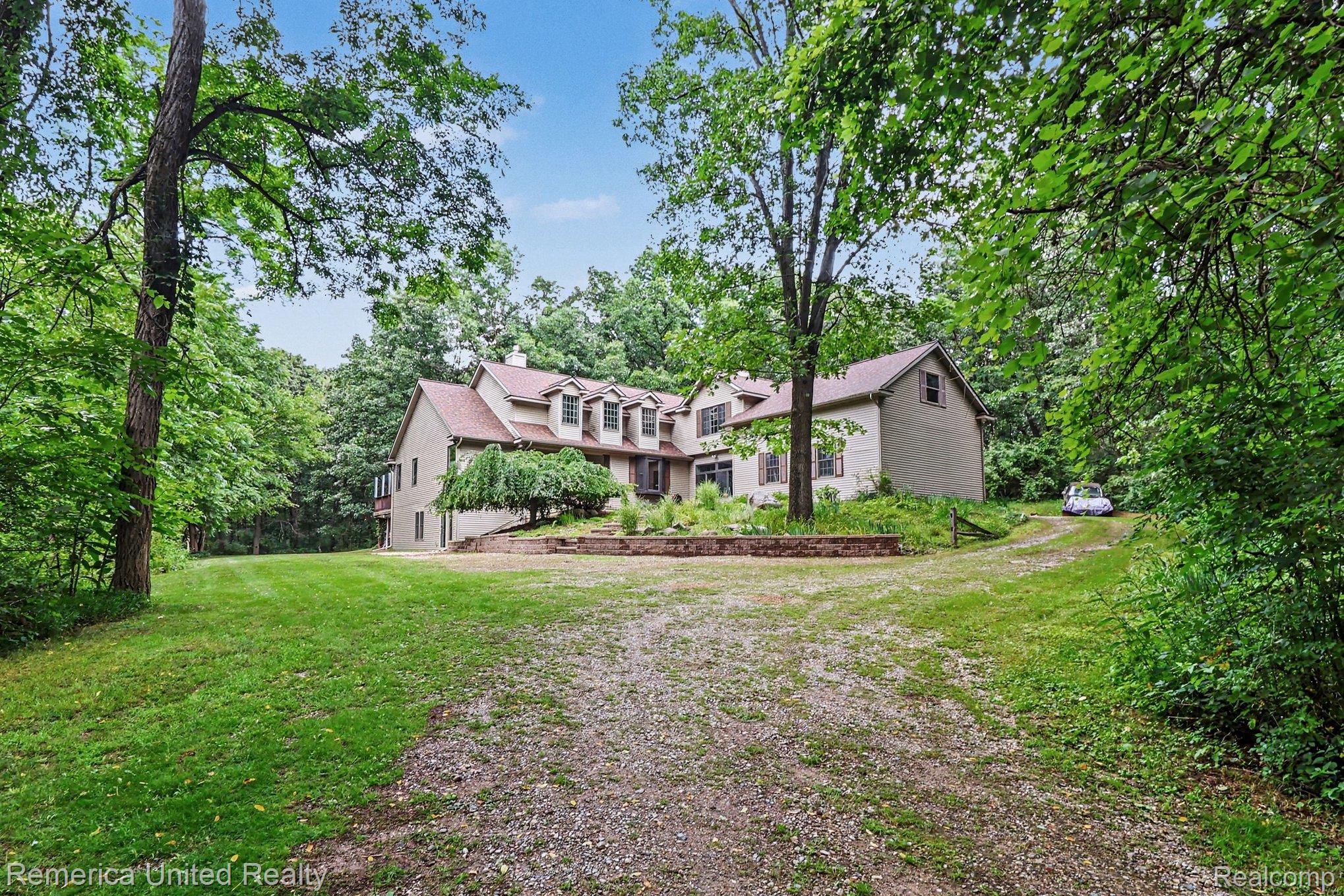 20962 Wasson Road Gregory, MI 48137 - Photo 3 of 39 Expansive property featuring a multi-story residence with dormer windows, a gravel driveway, and surrounding mature trees