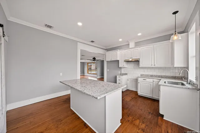 a kitchen with granite countertop a stove a sink and white cabinets with wooden floor