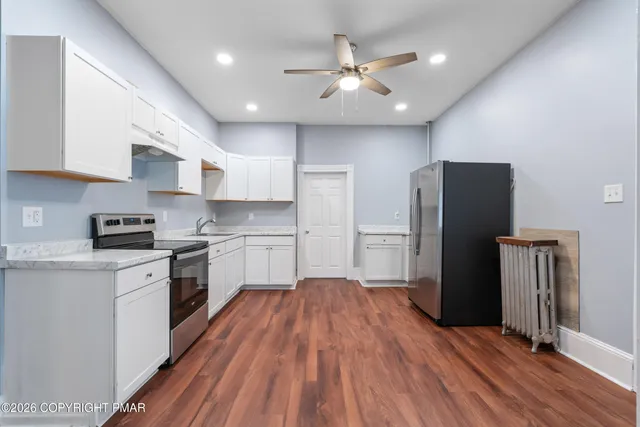 a kitchen with stainless steel appliances a refrigerator a sink dishwasher a stove and white cabinets with wooden floor