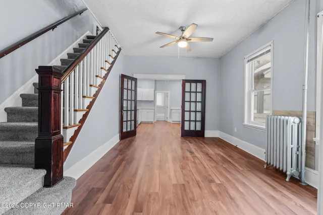 a view of an empty room with wooden floor and fan