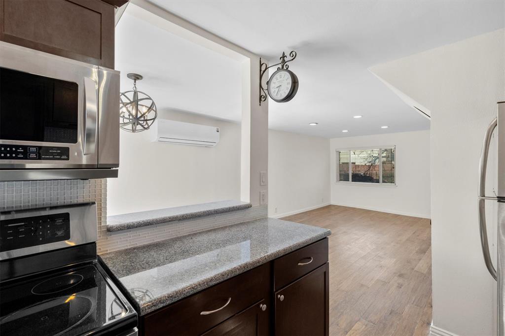 4039 Cole Avenue, Unit 105 Dallas, TX 75204 - Photo 14 of 39 Kitchen featuring light stone counters, light wood-style flooring, a wall mounted AC, appliances with stainless steel finishes, and dark brown cabinets
