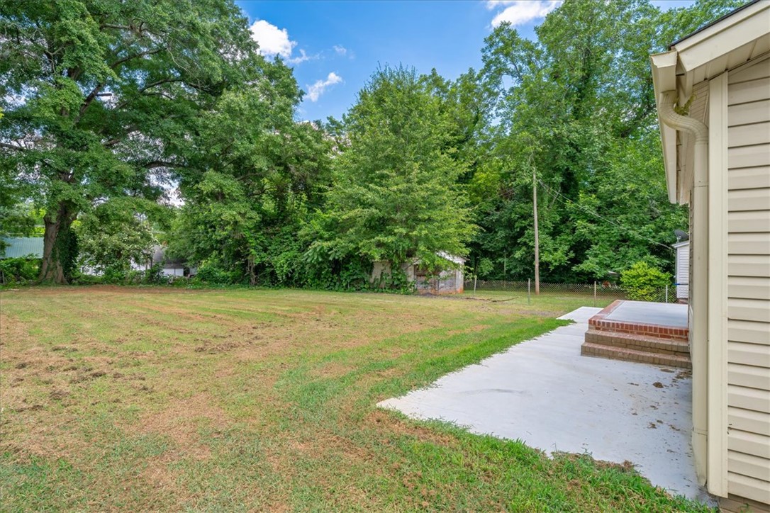 1102 West End Avenue Anderson, SC 29625 - Photo 26 of 28 A spacious grassy yard extends from a brick-stepped patio, bordered by mature trees and a distant shed.