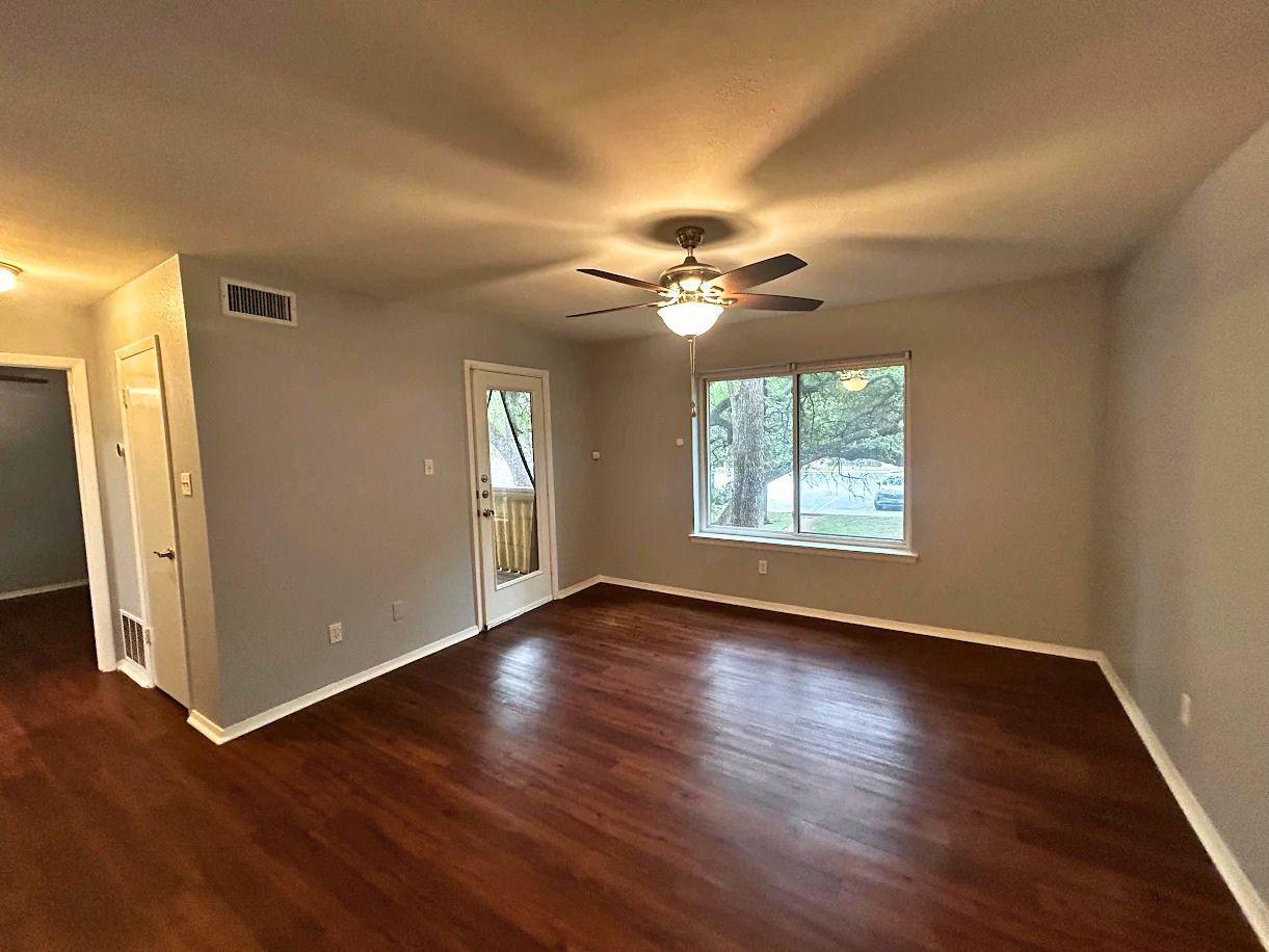 8210 Bent Tree Road, Unit 247 Austin, TX 78759 - Photo 2 of 21 Living area featuring rich hardwood floors, a large window providing natural light, and a ceiling fan with integrated lighting