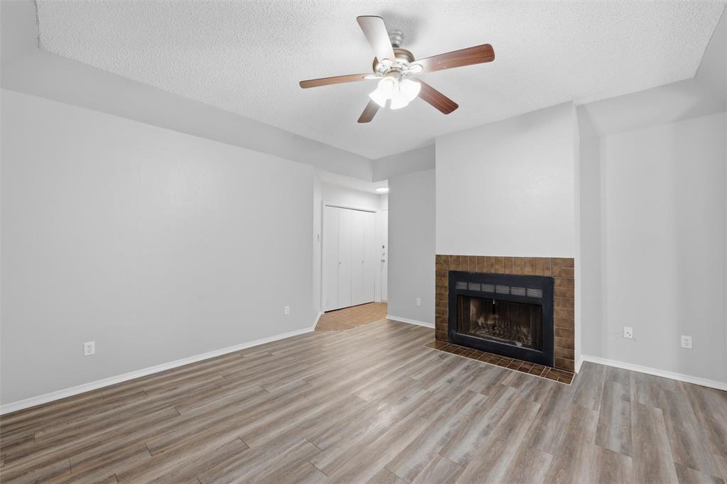 2332 Melissa Drive Waco, TX 76708 - Photo 4 of 15 Unfurnished living room featuring a ceiling fan, a textured ceiling, a fireplace, and light wood-type flooring