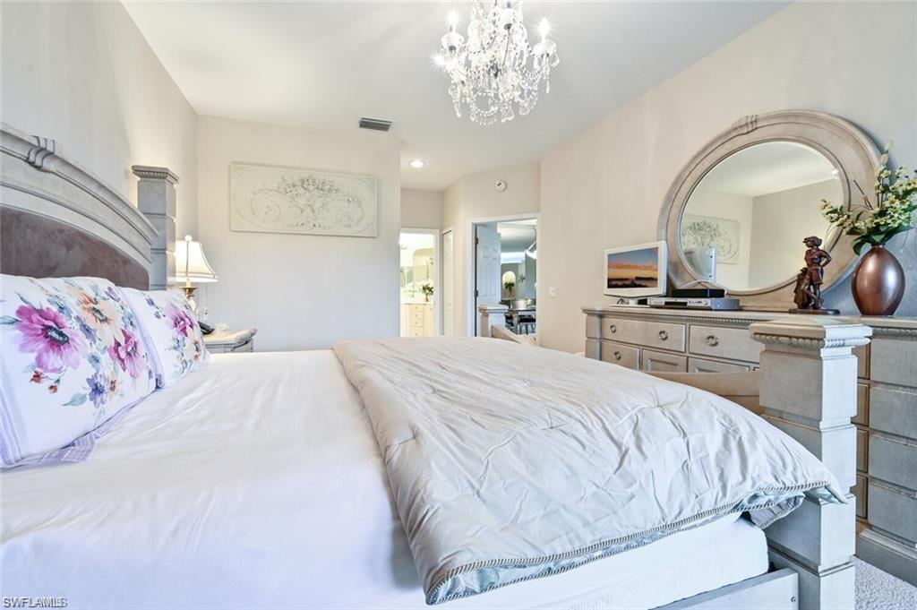 6065 Pinnacle Lane, Unit 1001 Naples, FL 34110 - Photo 18 of 26 a bedroom with a bed and a chandelier
