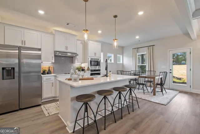 a kitchen with stainless steel appliances a dining table chairs stove refrigerator and wooden floor