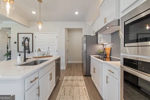 a large white kitchen with stainless steel appliances a sink and cabinets