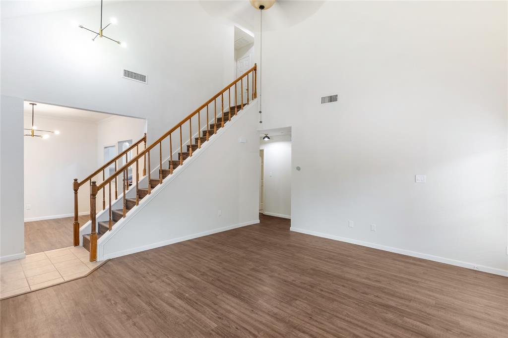 12680 Hillcrest Road, Unit 4101 Dallas, TX 75230 - Photo 3 of 37 Vaulted ceiling living area featuring a prominent staircase with wood railings, wood-finish flooring, and a modern chandelier