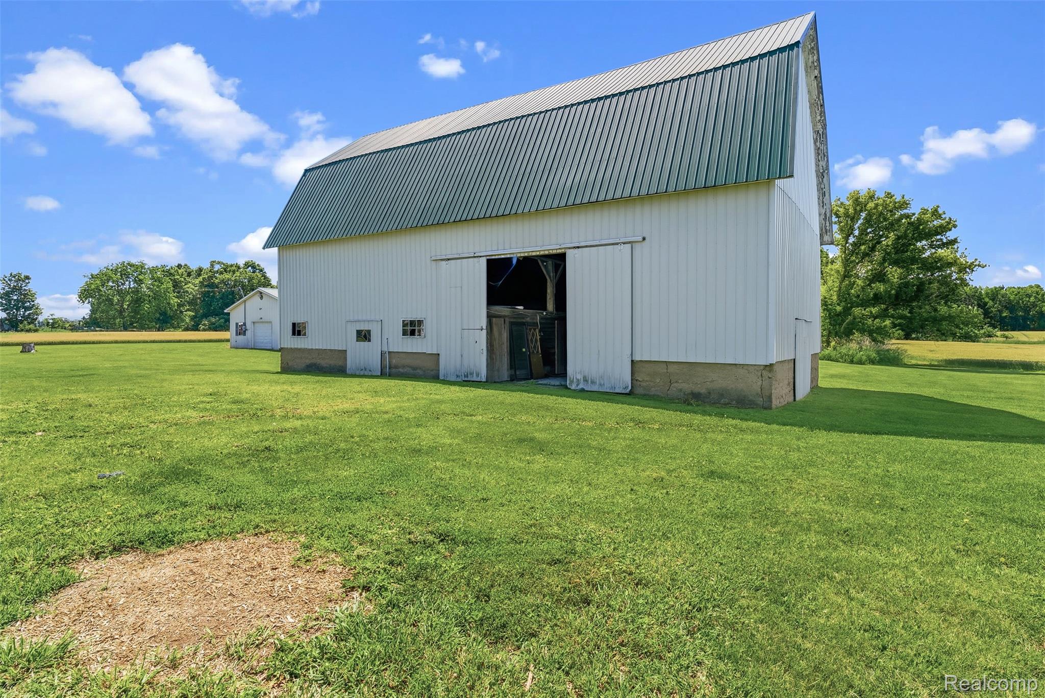 5843 West Dewey Road Owosso, MI 48867 - Photo 49 of 58 White barn with a green metal roof, featuring a large sliding door entry and multiple access doors