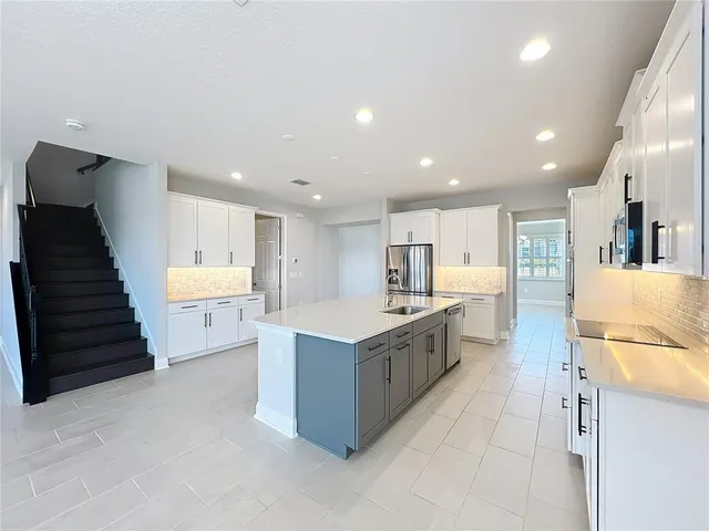 a large white kitchen with kitchen island a sink a stove a refrigerator and white cabinets with wooden floor