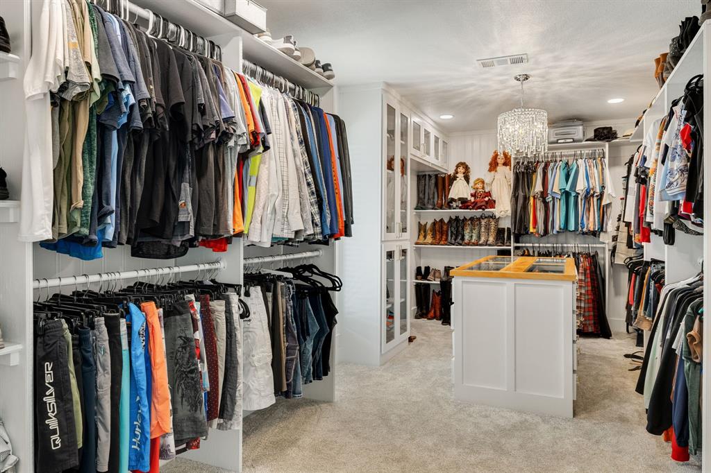 12240 Wellington Road Ponder, TX 76259 - Photo 25 of 40 Spacious custom closet featuring extensive built-in shelving, multiple hanging rods, a central island with a wood-finish countertop, recessed lighting, and a decorative chandelier