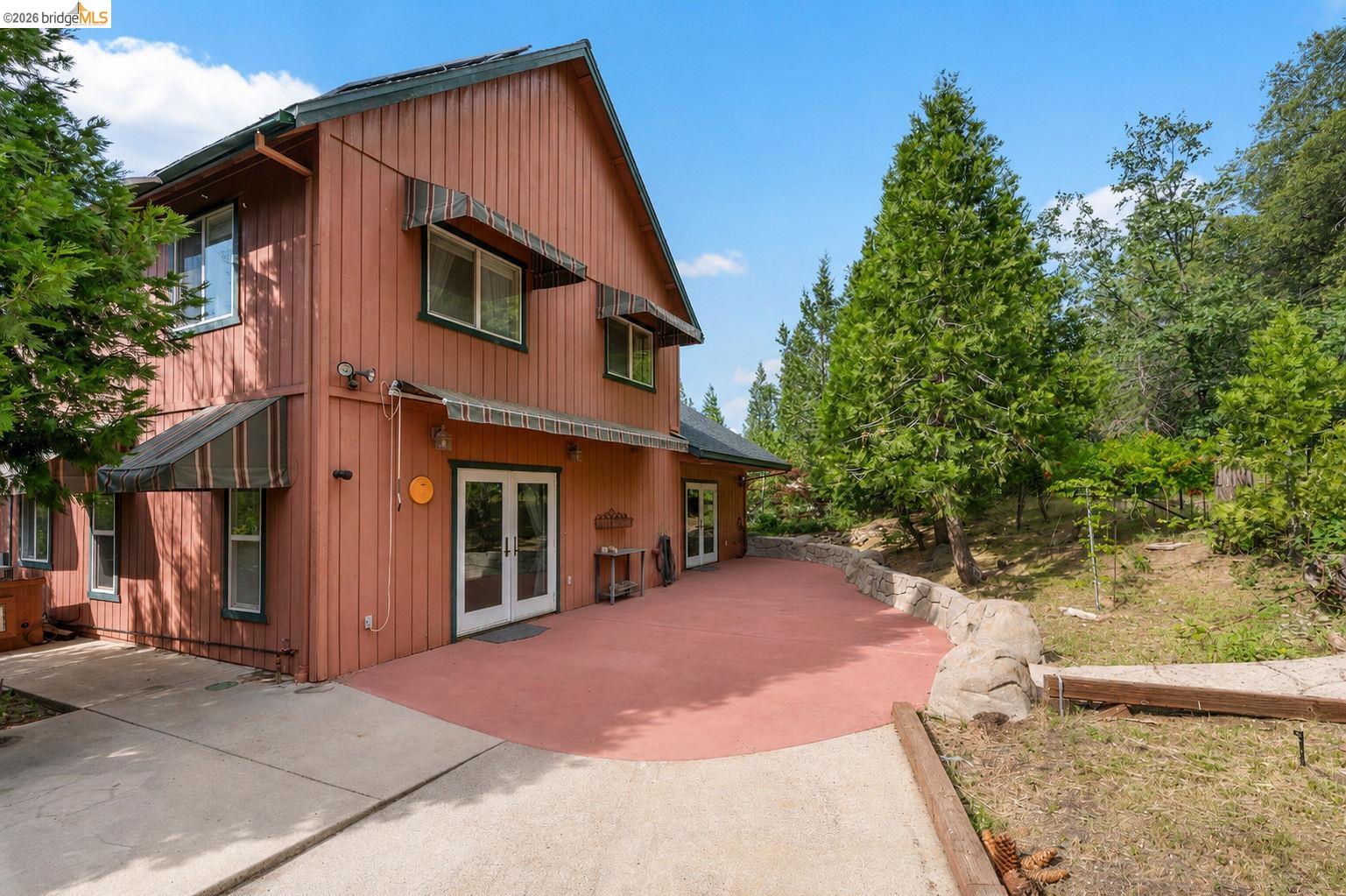 22401 Ridge Road Twain Harte, CA 95383 - Photo 33 of 56 Two-story exterior featuring board-and-batten siding, multiple windows with awning coverings, and double glass French doors opening onto a red-toned patio
