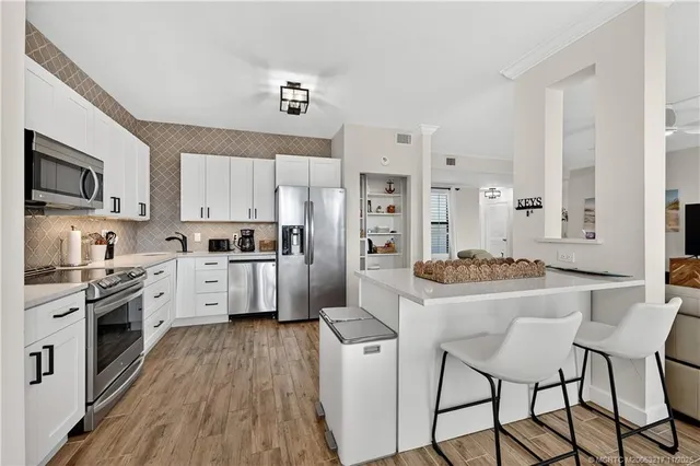 a kitchen with stainless steel appliances a stove a sink dishwasher a refrigerator with white cabinets and wooden floor