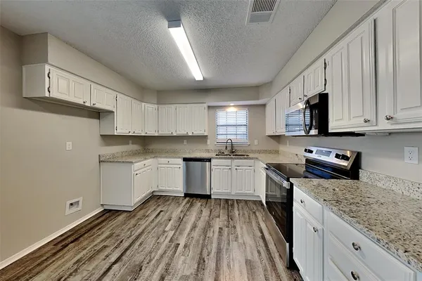 a kitchen with a sink dishwasher a stove top oven a refrigerator with white cabinets and wooden floor