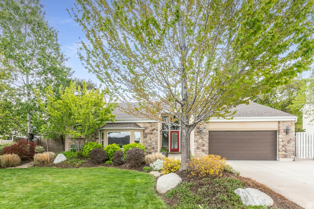 Stone facade residence featuring a two-car garage, mature trees, and established landscaping