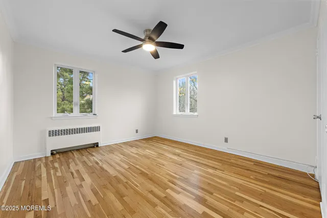 a view of empty room with wooden floor and fan