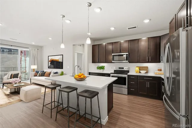 a kitchen with stainless steel appliances granite countertop a refrigerator a stove top oven a sink dishwasher a dining table and chairs with wooden floor