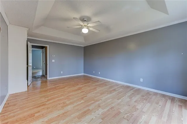 a view of an empty room with wooden floor and a ceiling fan