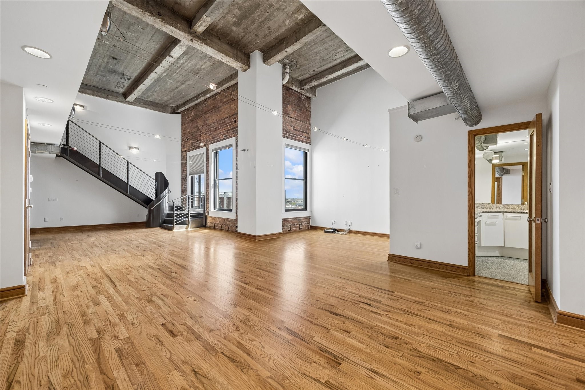 915 Franklin Street, Unit 9L Houston, TX 77002 - Photo 5 of 50 Light-filled loft featuring wood floors, soaring ceilings, and an exposed brick wall in the dining and living spaces.