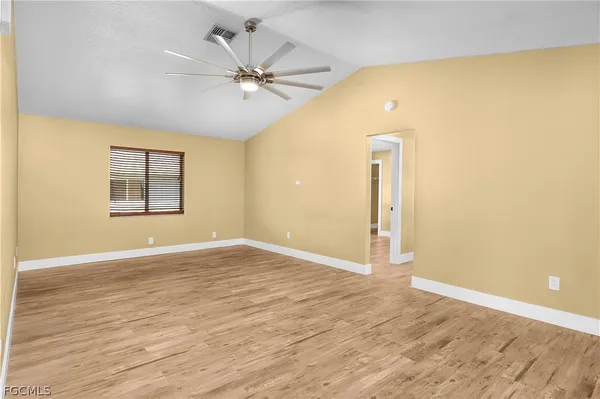 a view of an empty room with wooden floor and a ceiling fan