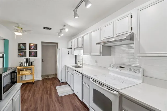 a kitchen with a sink dishwasher stove and white cabinets with wooden floor